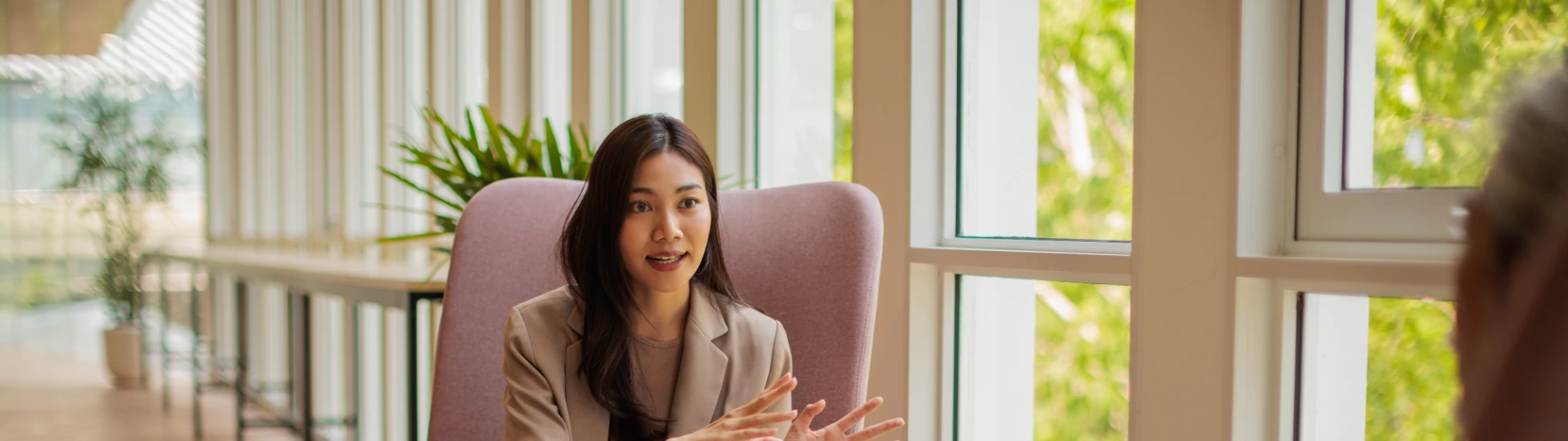 Asian Lady sitting in a chair talking to a colleague, sharing knowledge